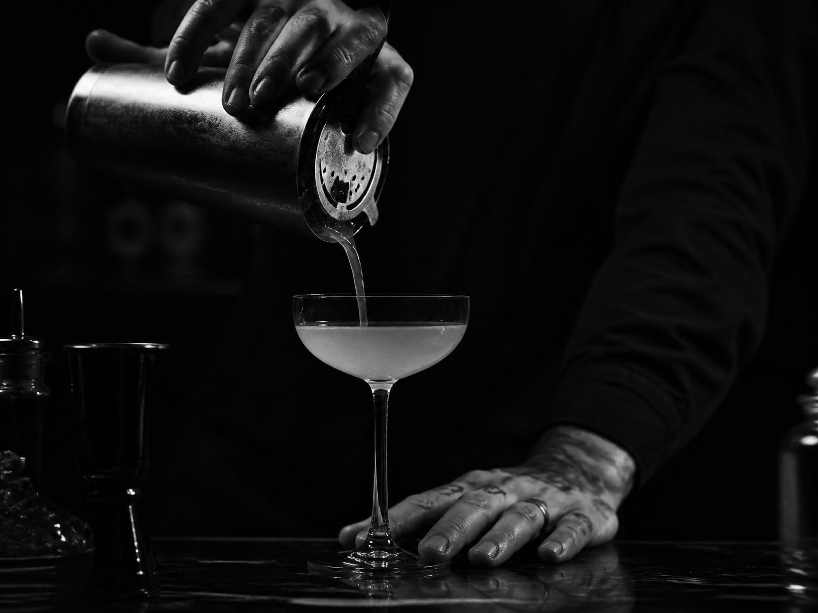 A bartender straining a cocktail into a coupe glass